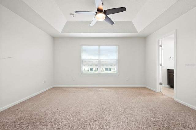 empty room featuring baseboards, a raised ceiling, light colored carpet, and a ceiling fan