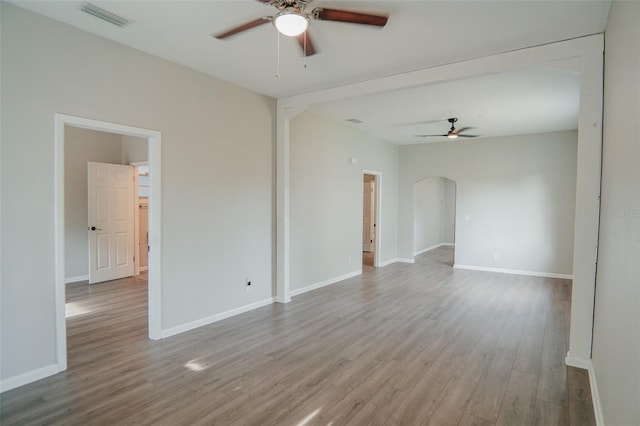 empty room featuring wood finished floors, visible vents, a ceiling fan, arched walkways, and baseboards