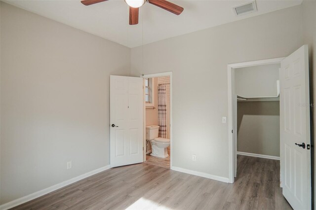 unfurnished bedroom with baseboards, visible vents, wood finished floors, a closet, and a walk in closet