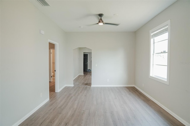 unfurnished room with light wood finished floors, arched walkways, a healthy amount of sunlight, visible vents, and a ceiling fan