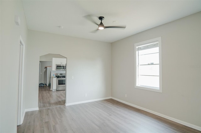 empty room featuring light wood finished floors, a ceiling fan, and baseboards