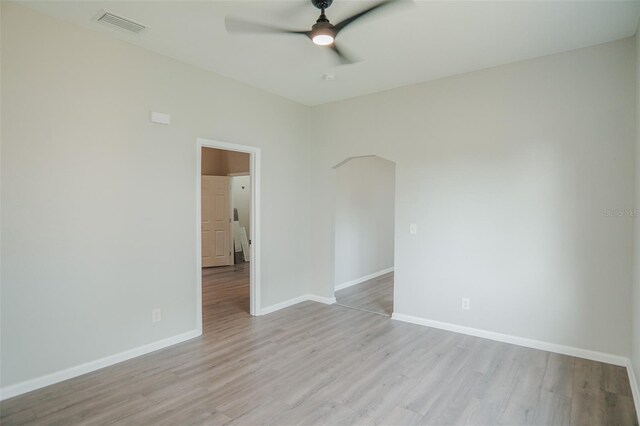 unfurnished room featuring light wood finished floors, arched walkways, baseboards, visible vents, and a ceiling fan