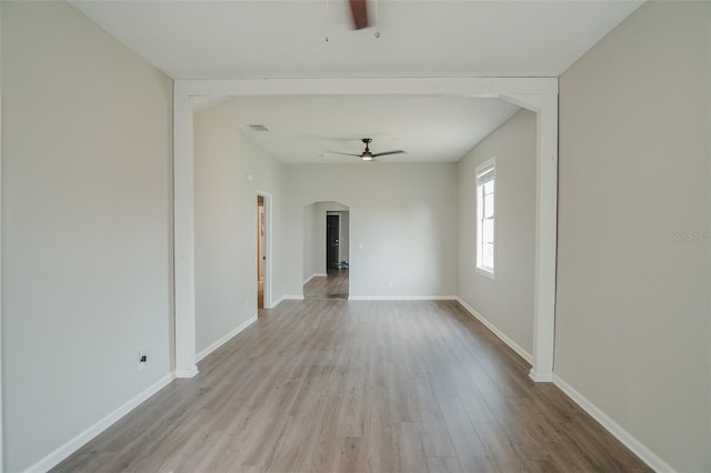 unfurnished room featuring arched walkways, visible vents, baseboards, a ceiling fan, and wood finished floors