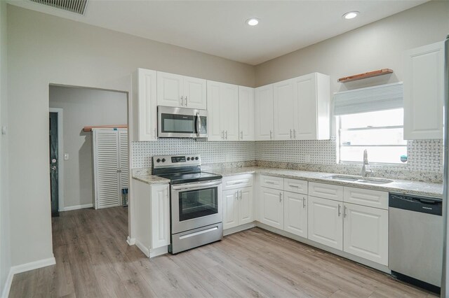 kitchen featuring white cabinets, stainless steel appliances, visible vents, a sink, and light wood-style floors