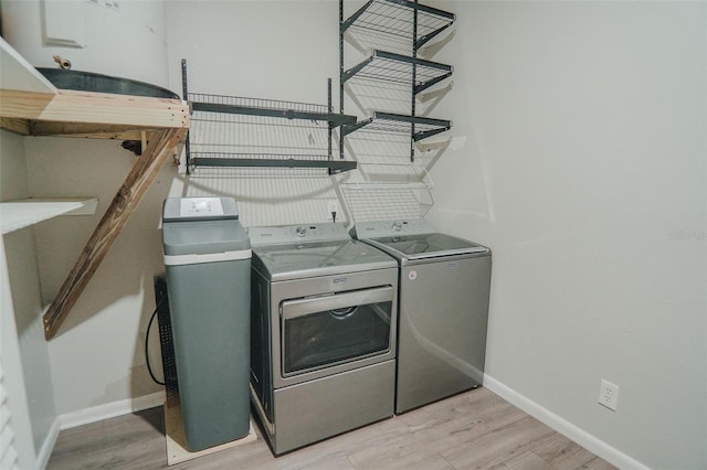clothes washing area featuring baseboards, laundry area, light wood-style flooring, and washer and clothes dryer