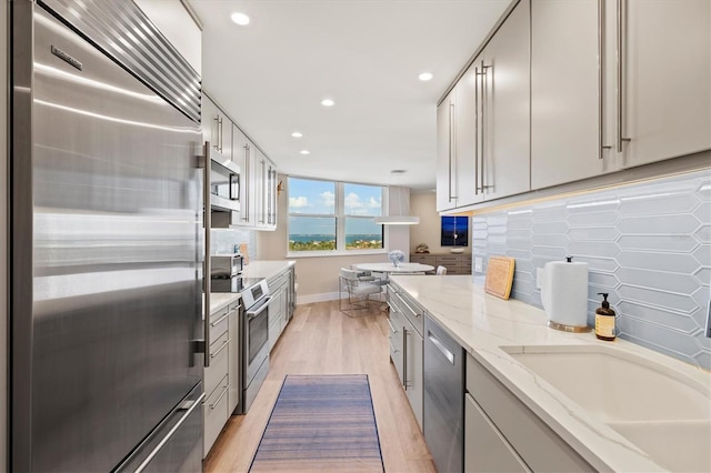 kitchen with tasteful backsplash, light wood-type flooring, light stone counters, recessed lighting, and stainless steel appliances