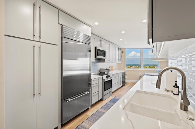 kitchen with tasteful backsplash, a sink, appliances with stainless steel finishes, recessed lighting, and light wood-style flooring