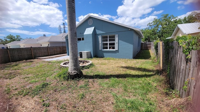 back of property with a fenced backyard, stucco siding, central AC, and a lawn