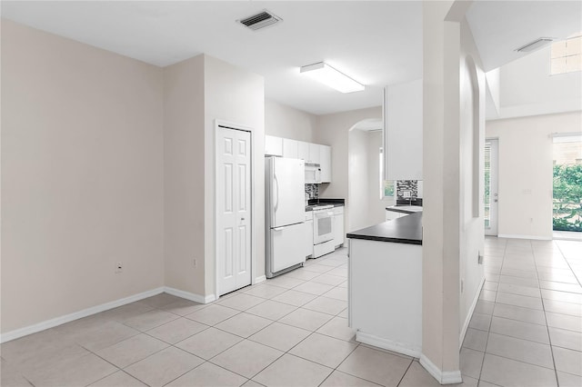 kitchen featuring visible vents, white cabinets, arched walkways, dark countertops, and white appliances