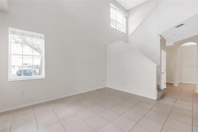 unfurnished living room featuring visible vents, baseboards, arched walkways, stairway, and light tile patterned flooring