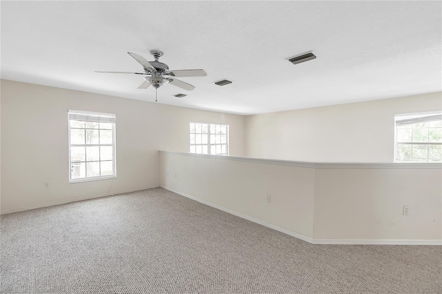 unfurnished room with a wealth of natural light, visible vents, a ceiling fan, and carpet floors