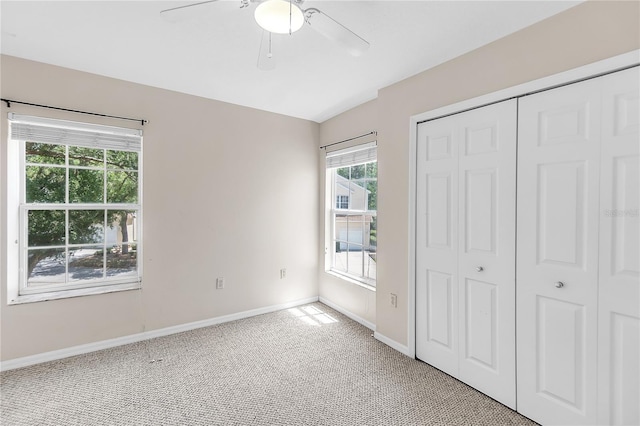 unfurnished bedroom featuring baseboards, vaulted ceiling, a closet, light carpet, and ceiling fan