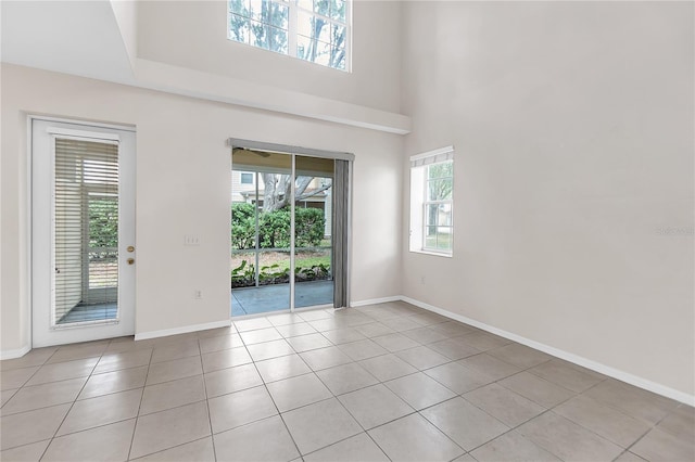 unfurnished room with light tile patterned flooring, baseboards, and a towering ceiling