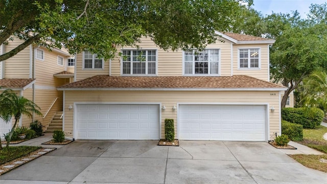 view of property with a shingled roof, concrete driveway, a garage, and stairs
