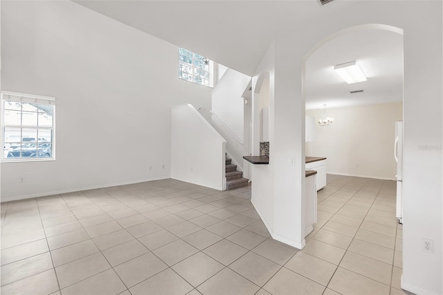 interior space featuring light tile patterned floors, baseboards, arched walkways, a chandelier, and stairway