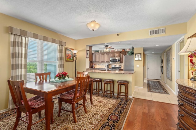 dining area featuring a textured ceiling, visible vents, baseboards, ceiling fan, and light wood-style floors