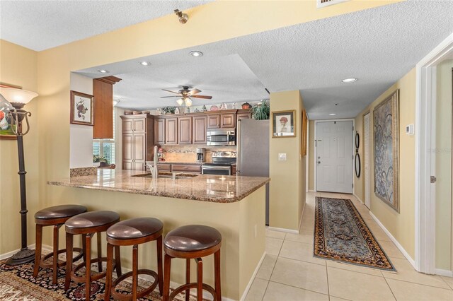kitchen featuring a kitchen bar, decorative backsplash, a sink, a peninsula, and appliances with stainless steel finishes