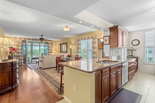 kitchen with a sink, stone countertops, a kitchen bar, light wood-style floors, and ceiling fan