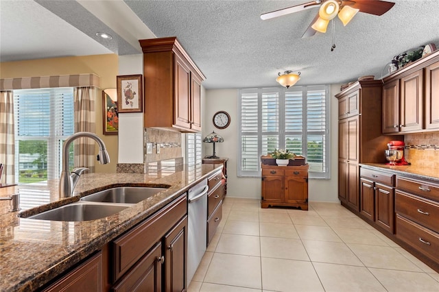 kitchen with a sink, dishwasher, light tile patterned floors, ceiling fan, and dark stone counters