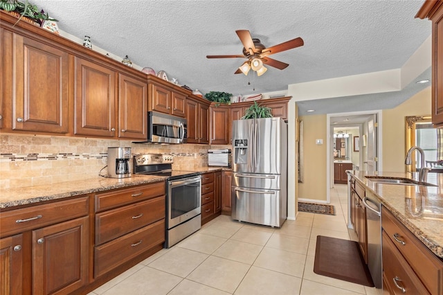 kitchen with a sink, light tile patterned flooring, a ceiling fan, light stone countertops, and appliances with stainless steel finishes