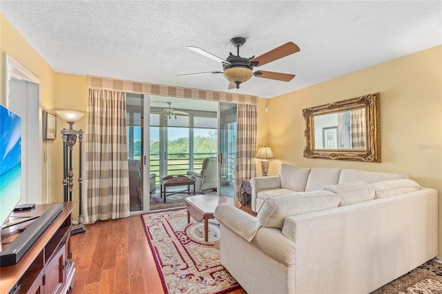living room with a textured ceiling, ceiling fan, and light wood finished floors