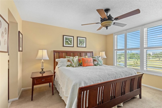 bedroom featuring light carpet, baseboards, ceiling fan, and a textured ceiling