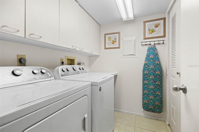 washroom featuring light tile patterned flooring, washing machine and clothes dryer, a textured ceiling, baseboards, and cabinet space