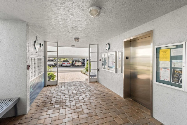 hallway with elevator, brick floor, and a textured wall