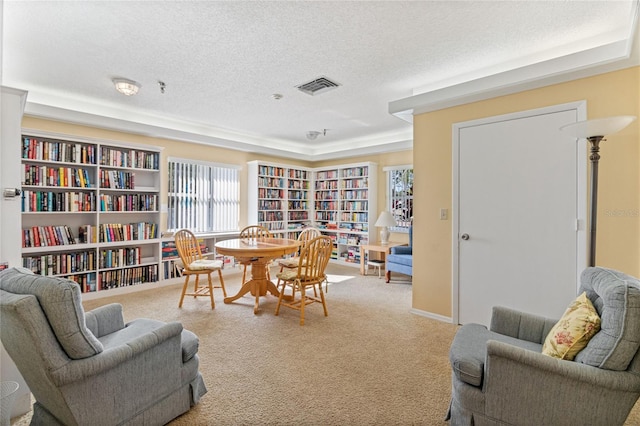 living area with visible vents, bookshelves, carpet, and a textured ceiling