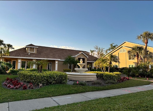 view of front facade featuring a front yard, stucco siding, and roof with shingles
