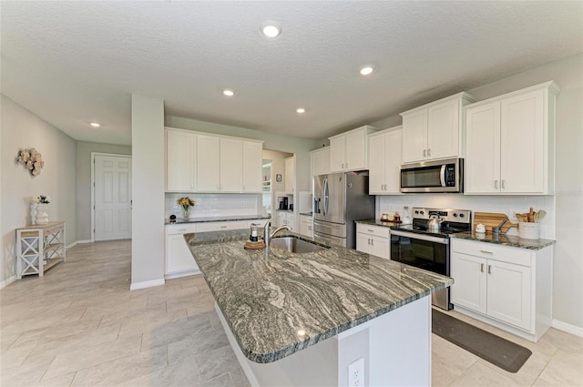 kitchen with stainless steel appliances, backsplash, a sink, a center island with sink, and dark stone counters