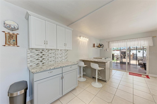 3053 Monica Pkwy, Sarasota, FL 34234 - kitchen featuring decorative backsplash, light tile patterned floors, white cabinets, baseboards, and light stone countertops