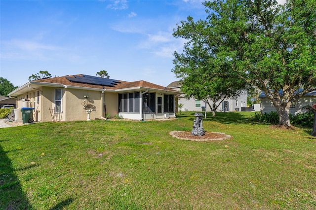 3459 Lotus Rd, North Port, FL 34291 - back of house with roof mounted solar panels, stucco siding, a sunroom, and a lawn