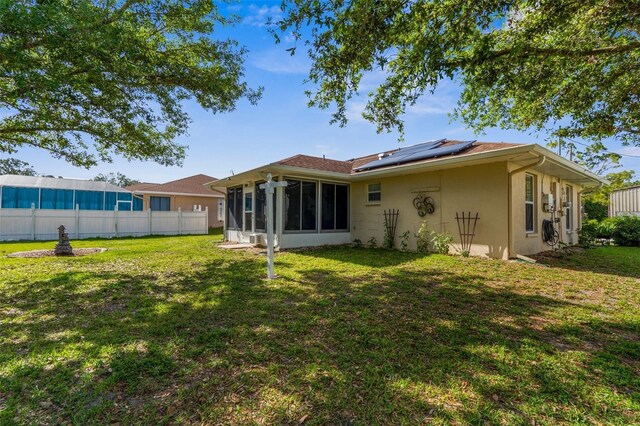 3459 Lotus Rd, North Port, FL 34291 - rear view of house featuring stucco siding, fence, solar panels, a sunroom, and a yard