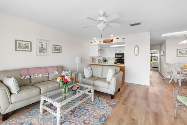 living room featuring light wood finished floors, a ceiling fan, visible vents, and recessed lighting