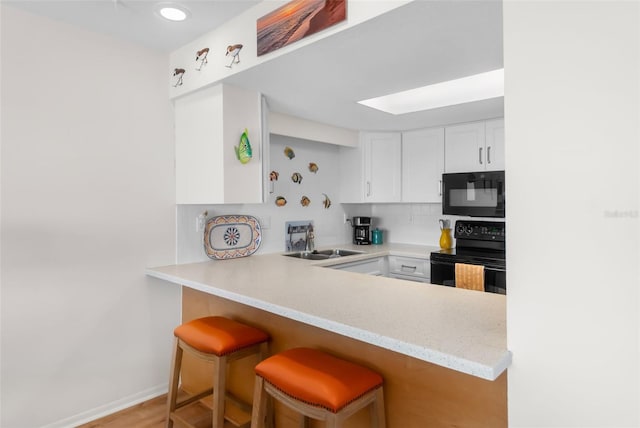 kitchen with white cabinets, a peninsula, a sink, a kitchen bar, and black appliances