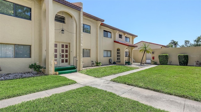 view of front of property featuring stucco siding, a tiled roof, fence, and a front lawn