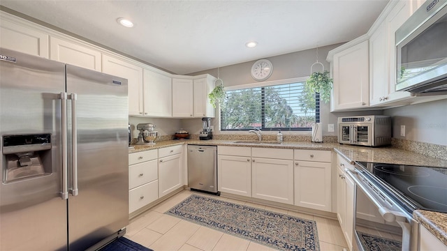 kitchen with a sink, light stone countertops, white cabinetry, and stainless steel appliances