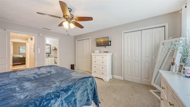 bedroom featuring baseboards, light carpet, two closets, visible vents, and ceiling fan