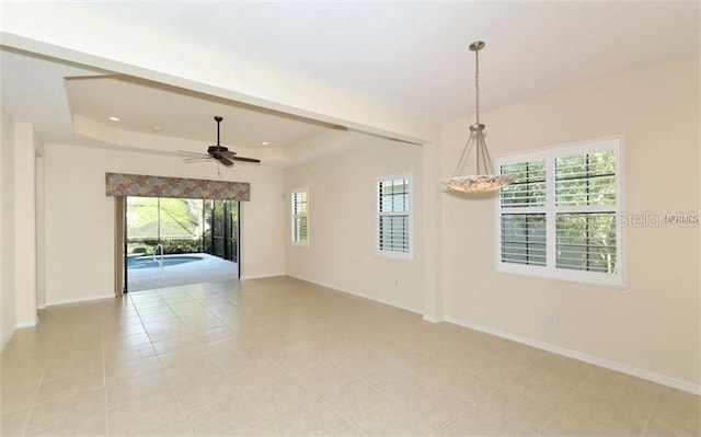 empty room with a raised ceiling, ceiling fan, plenty of natural light, and baseboards