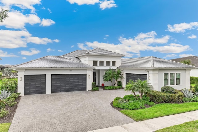 prairie-style house featuring an attached garage, stucco siding, a tile roof, and decorative driveway