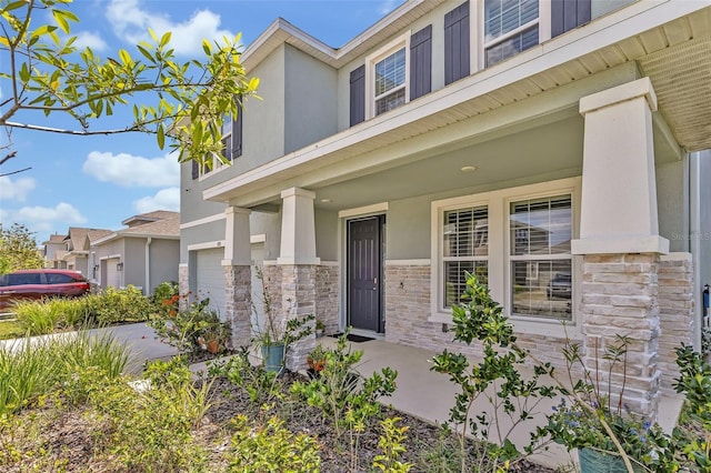 entrance to property featuring a porch, stucco siding, stone siding, and an attached garage