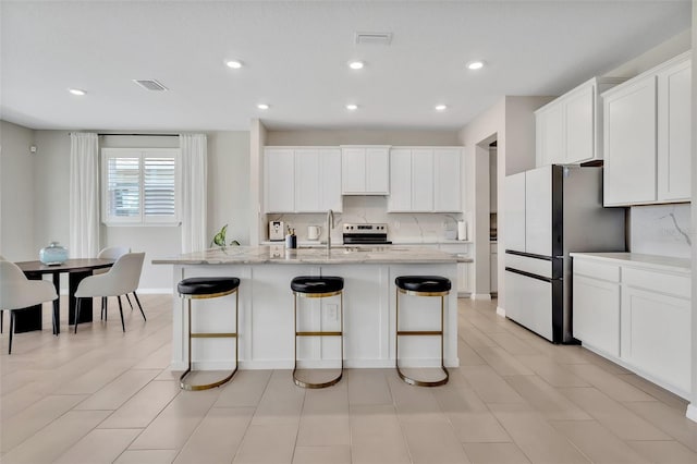 kitchen featuring tasteful backsplash, freestanding refrigerator, white cabinetry, and visible vents