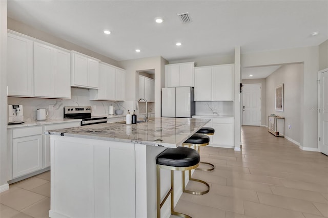 kitchen featuring freestanding refrigerator, visible vents, stainless steel range with electric cooktop, decorative backsplash, and a sink
