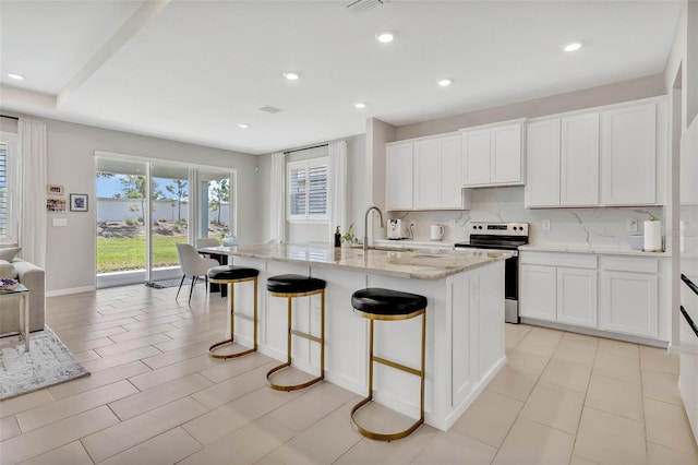 kitchen featuring a breakfast bar, light stone counters, stainless steel electric stove, decorative backsplash, and a sink