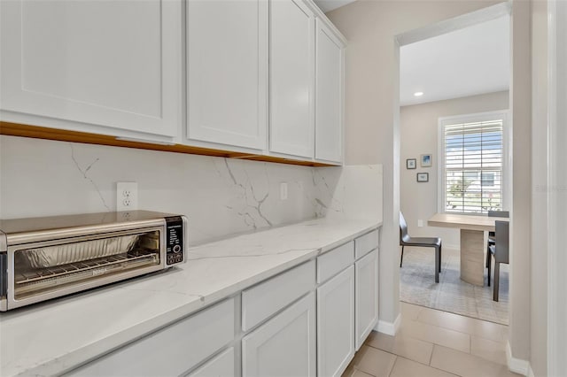 kitchen with backsplash, light tile patterned floors, light stone countertops, white cabinets, and a toaster