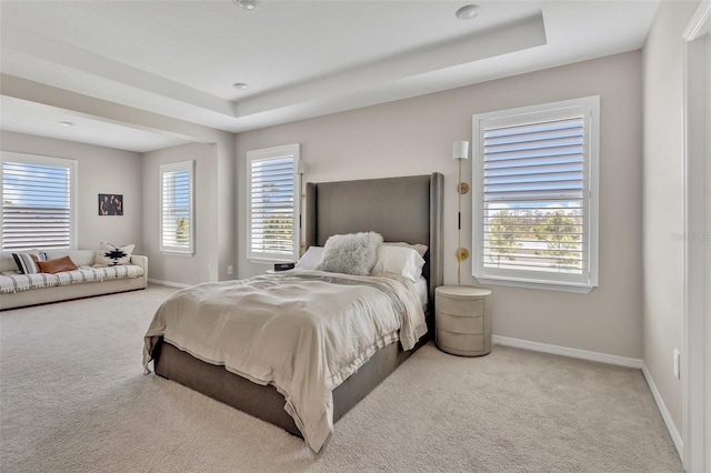 carpeted bedroom with multiple windows, baseboards, and a raised ceiling