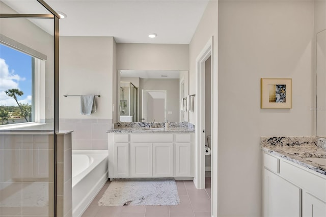 full bath with tile patterned floors, a garden tub, a stall shower, and two vanities
