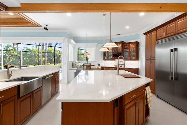 2196 Muskogee Trl, Nokomis, FL 34275 - kitchen featuring stainless steel appliances, a sink, brown cabinetry, an island with sink, and glass insert cabinets