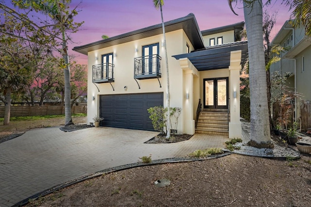 view of front of house with french doors, a garage, stucco siding, and a balcony